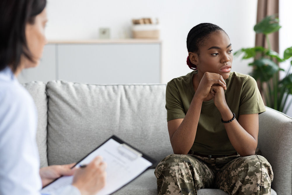 Woman in military fatigues looking off while reporting details to psychologist.