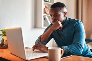 Man researching opioids in the bosdy on a laptop with coffee cup next to a laptop.