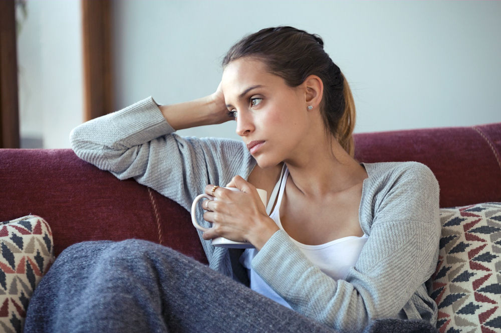 Woman holding coffee and looking out a window while thinking about addiction recovery