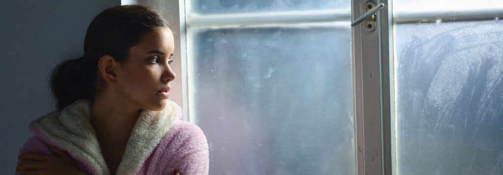 Young stoner woman looking out the window, worried about if you can get addicted to smoking weed