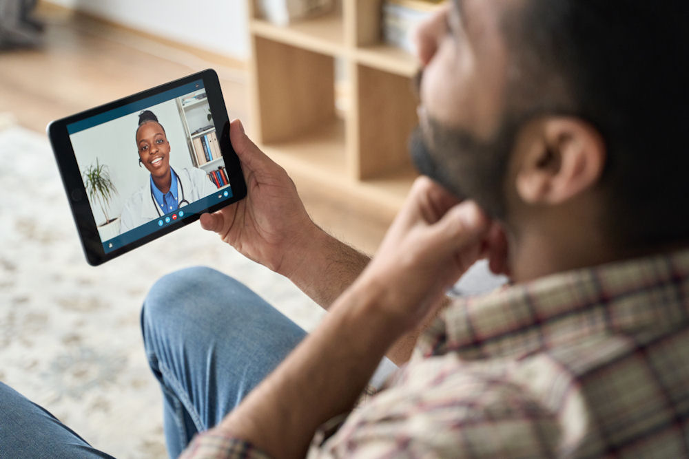 Man thinking while speaking to doctor on tablet during telehealth appointment.